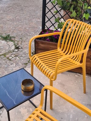 A yellow chair and a small table with a bowl on it, placed on a cobblestone surface. - Be Magenta Art Home - Yellow style (Magenta)