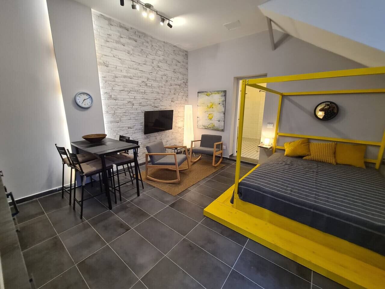 Une pièce compacte comprenant un lit superposé, une table à manger avec des chaises, un téléviseur à écran plat fixé au mur et une petite table d’appoint.