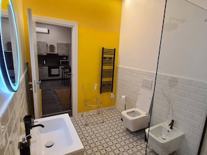 A bathroom with a white sink, toilet, and bidet, a mirror, and a yellow wall.
