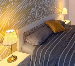 Ein ordentlich bezogenes Bett mit gestreifter Bettwäsche, einem gemusterten Kopfteil und zwei Nachttischlampen.