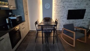 A modern kitchen with a dining area, featuring a brick wall, a clock, and a flat-screen TV mounted on the wall. - Be Magenta Art Home - Yellow style (Magenta)