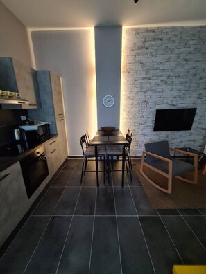 A modern kitchen with a dining area, featuring a brick wall, a clock, and a flat-screen TV mounted on the wall. - Be Magenta Art Home - Yellow style (Magenta)