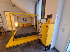 A modern bedroom with a bed under a yellow canopy, a small cabinet, and a clock on the wall. - Be Magenta Art Home - Yellow style (Magenta)