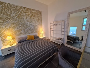 A modern bedroom with a bed, bedside lamps, a wardrobe, and a large mirror.