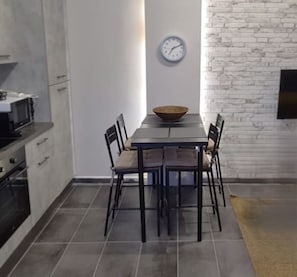 A modern kitchen with a dining table, chairs, a microwave, and a clock on the wall.