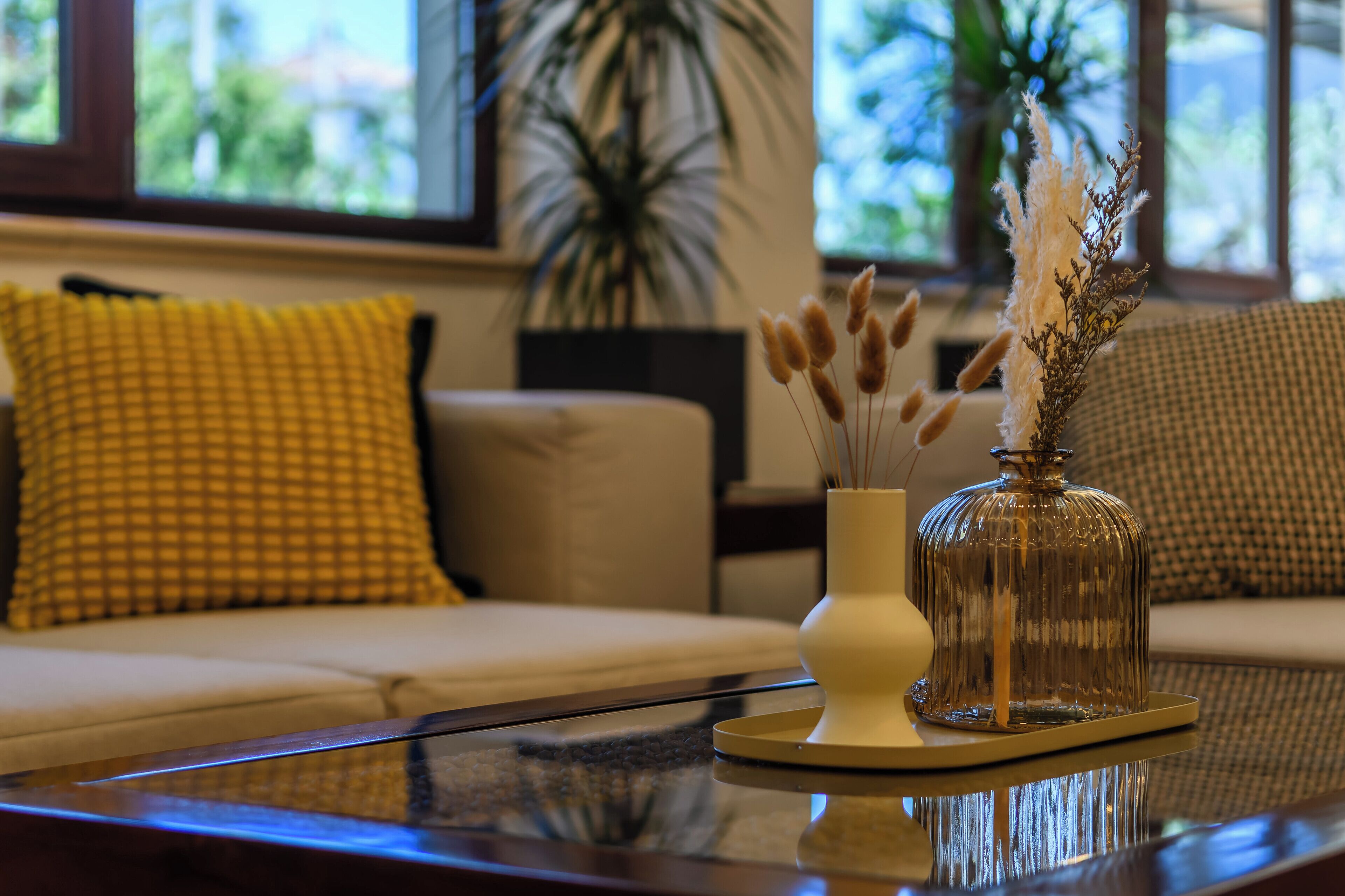 A modern living room with a glass coffee table, a white vase with dried plants, and a decorative glass dome on the table.