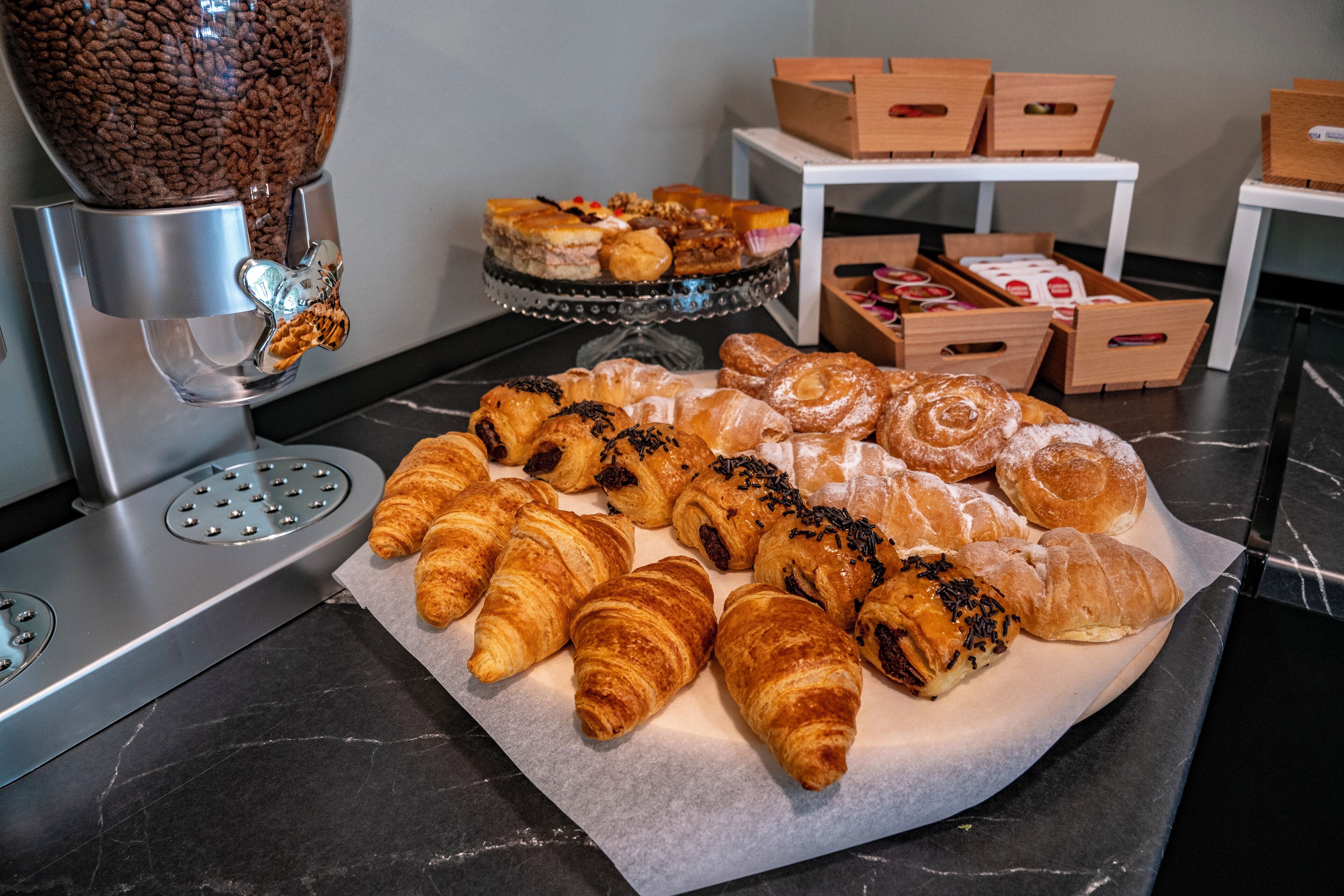 A display of assorted pastries on a marble countertop with a coffee machine and storage boxes in the background.