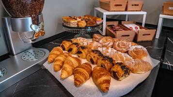 A display of assorted pastries on a marble countertop with a coffee machine and storage boxes in the background.