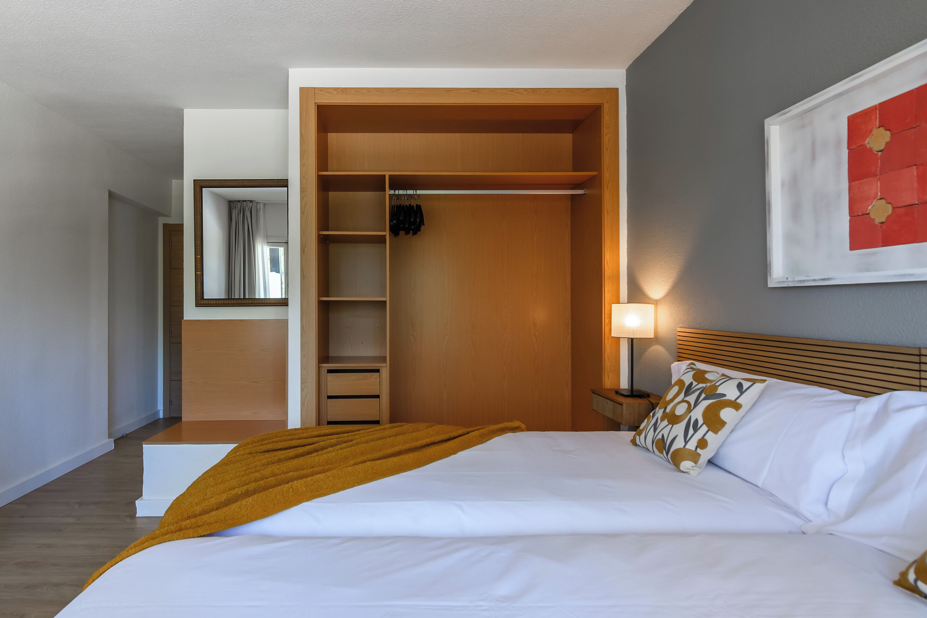 Una habitación de hotel con una cama, un armario, un espejo, una mesita de noche y una obra de arte en la pared.