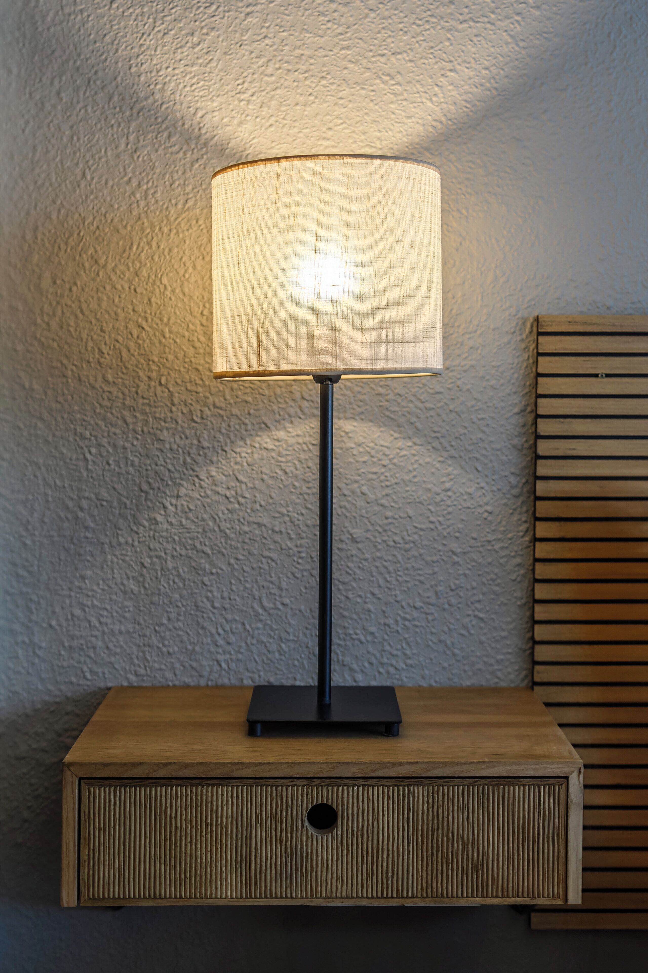 Una mesita de noche rectangular de madera con una lámpara negra encima.