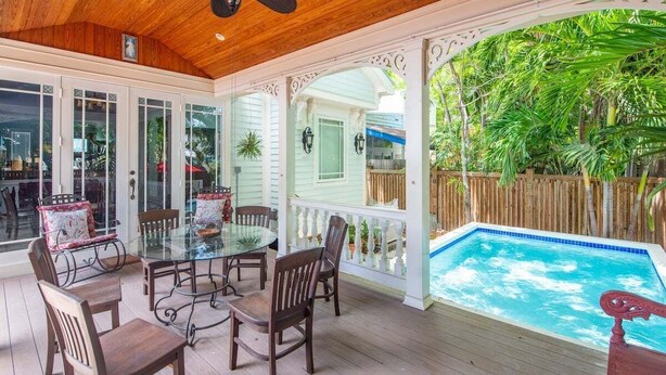 A covered patio with a glass table and chairs, a pool, and a wooden deck. - Casa De Cubana | New! Cuban-Style Home Near Duval (Key West)