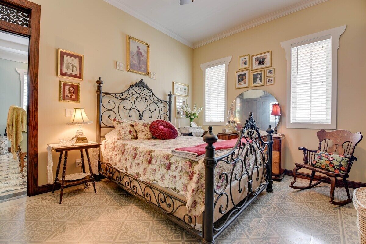 Une chambre à coucher avec un lit à baldaquin, une chaise en bois, une petite table avec une lampe et un miroir au mur.