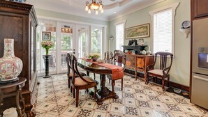 A dining area with a large wooden table, chairs, and a chandelier. There is a kitchen area with cabinets and a refrigerator. - Casa De Cubana | New! Cuban-Style Home Near Duval (Key West)