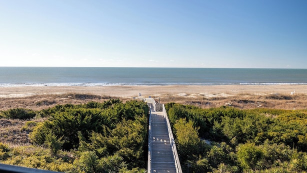 A coastal walkway leading to a beach with a clear view of the ocean.