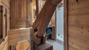 Un intérieur en bois avec des toilettes en bois, une douche et une étagère en bois où sont posées des serviettes.