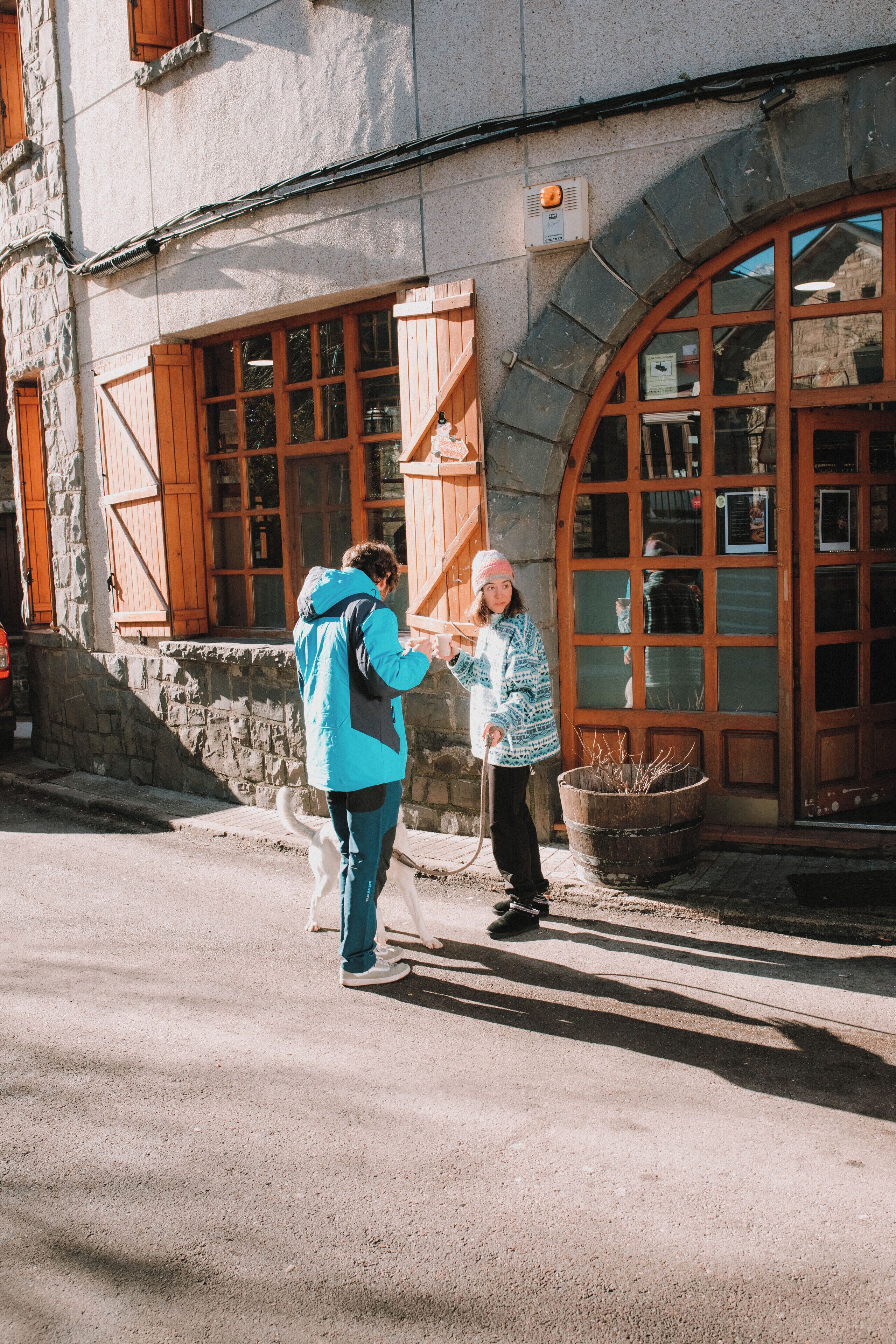 A building with stone walls and wooden shutters, a large arched window, and a dog on a leash.