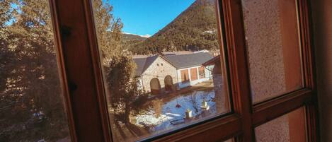 A view through a window of a building with a stone facade, arched windows, and a snow-covered courtyard.
