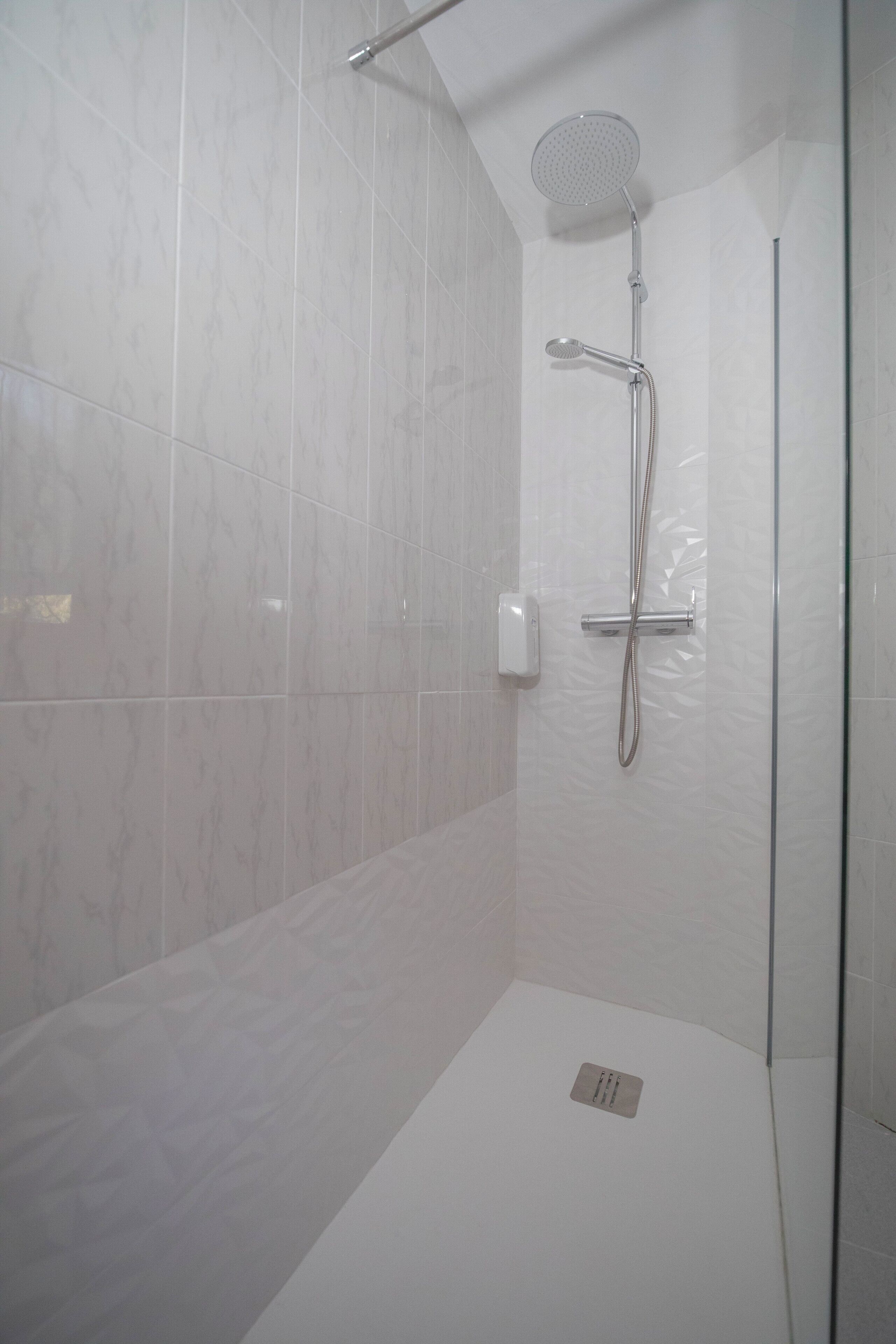 A modern shower with a handheld showerhead and a wall-mounted control panel.