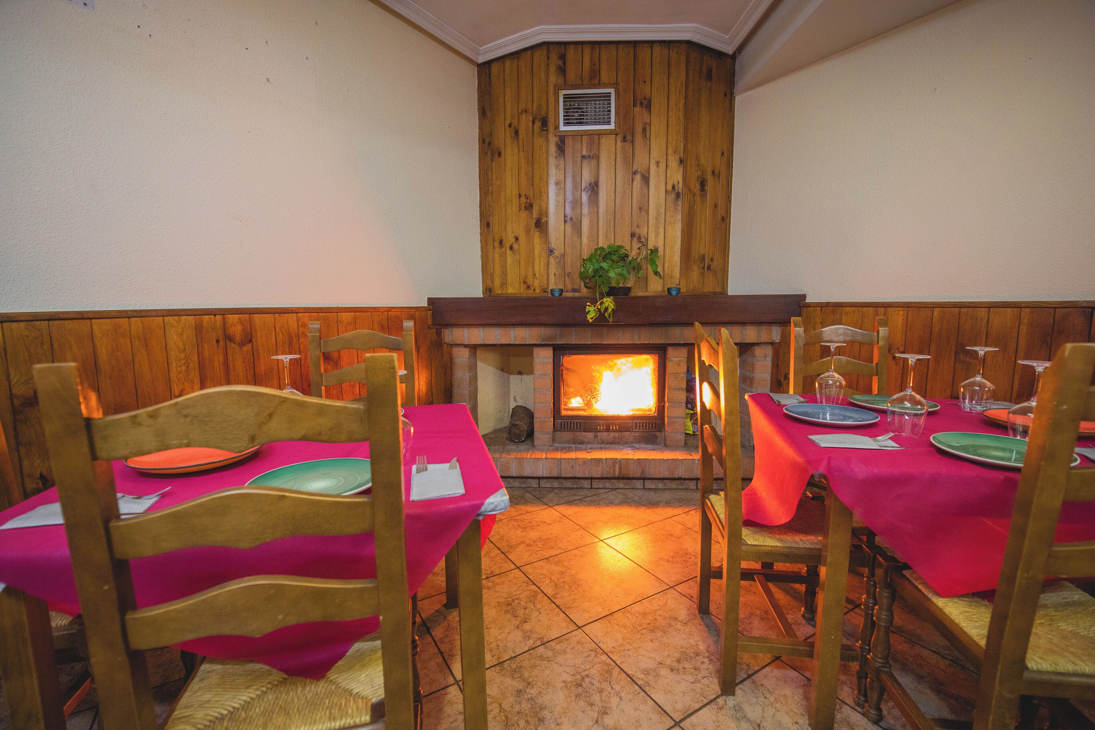 A dining area with wooden panel walls, a fireplace, and tables set with pink tablecloths and green plates.