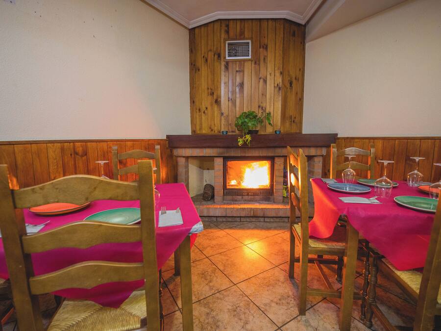 Un comedor con paneles de madera, chimenea y mesas dispuestas con manteles rosas y platos verdes.