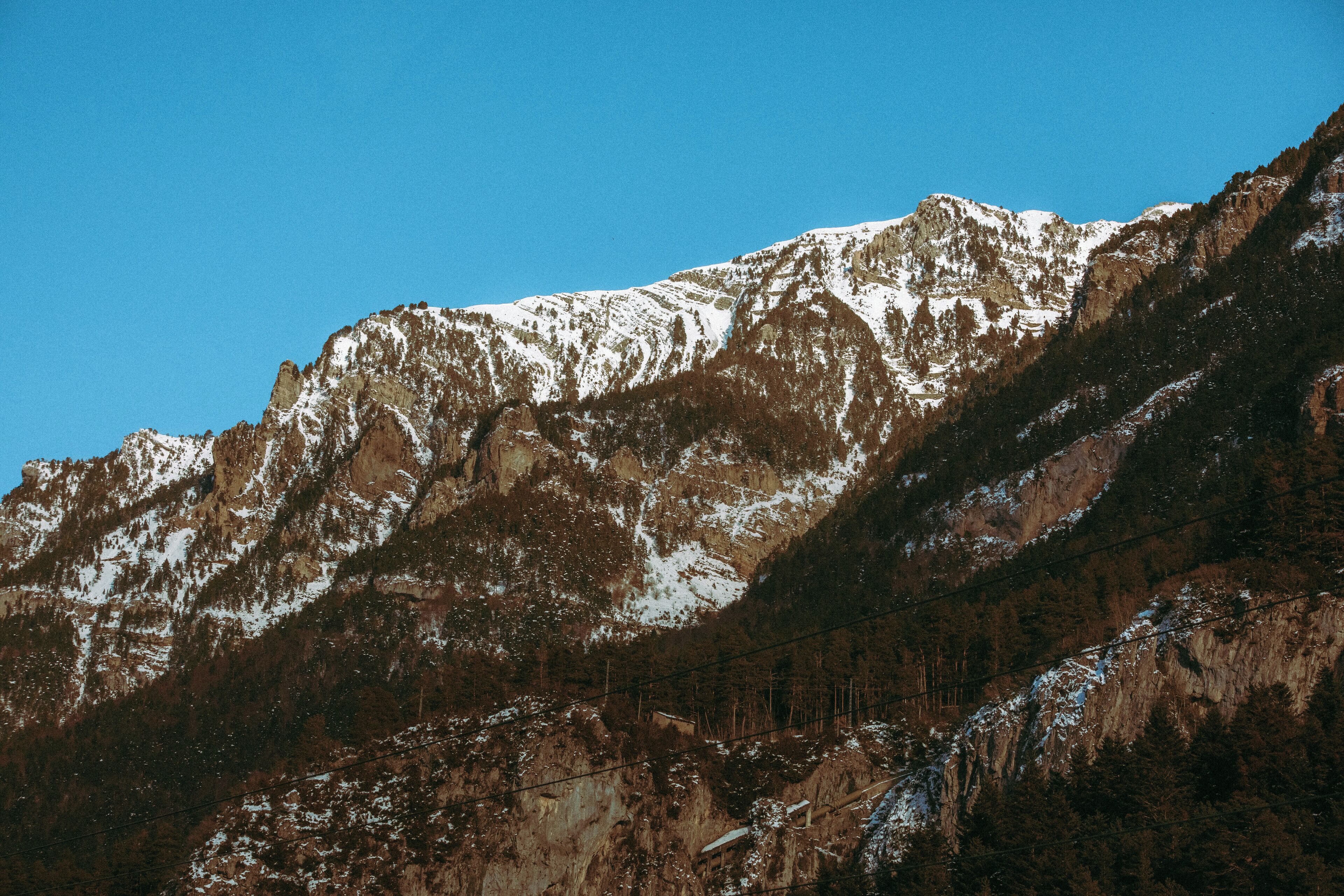 A mountain with snow-covered peaks and a forested slope.