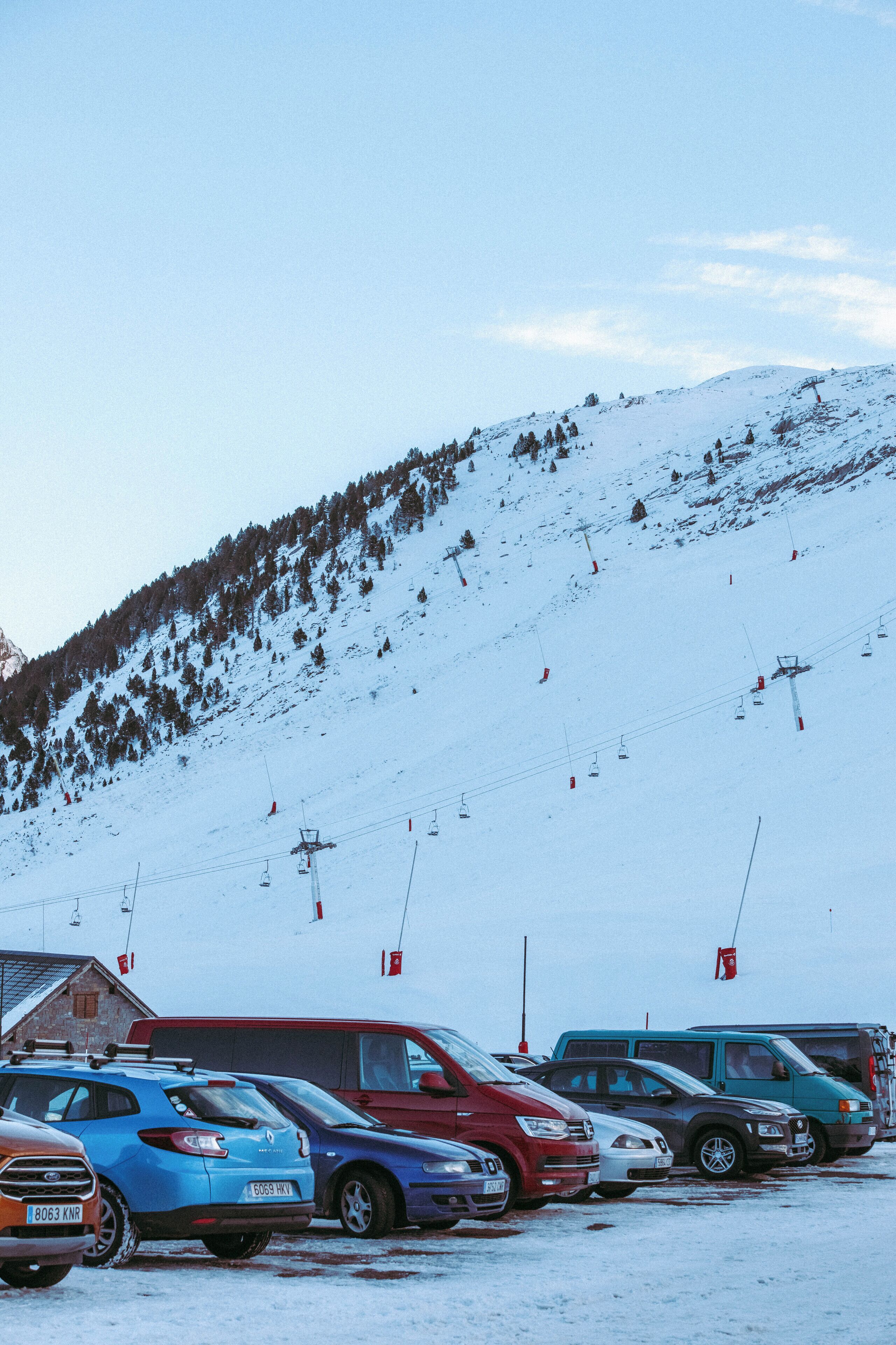 A parking lot with several cars and a ski lift in the background.