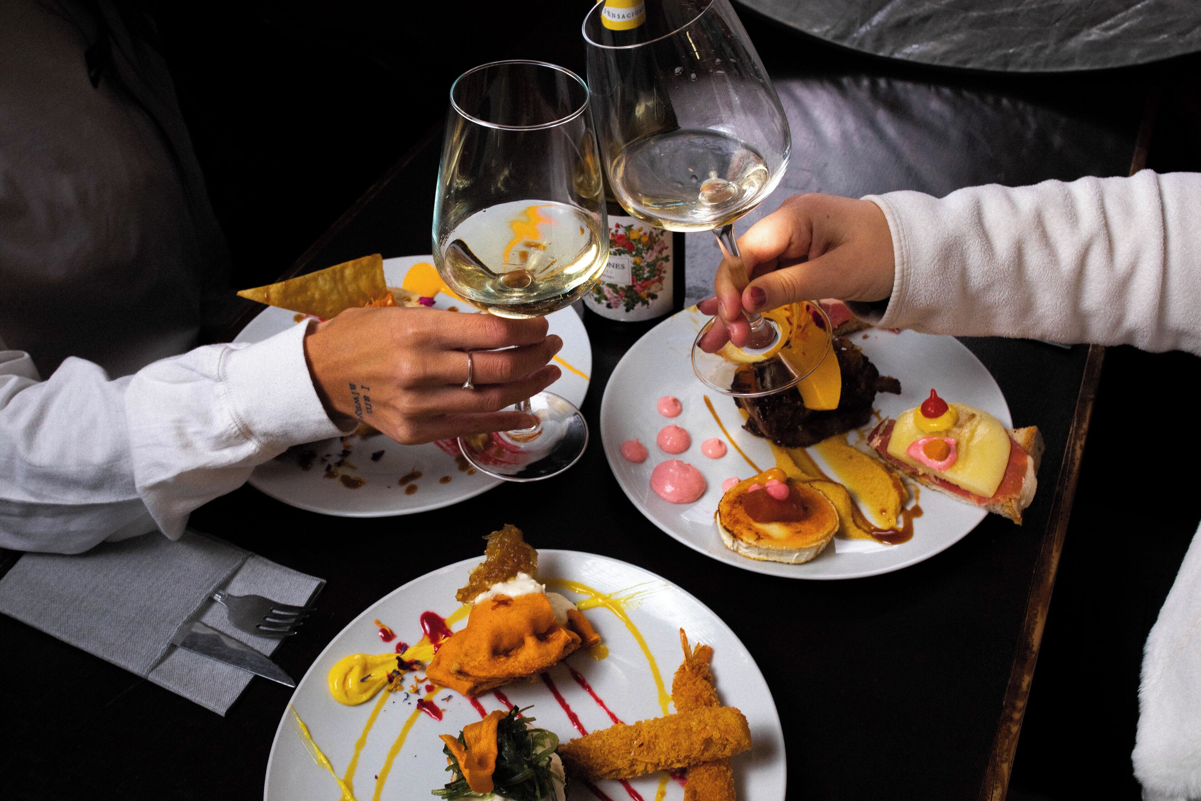 Una mesa de comedor con platos de comida y dos copas de vino blanco.