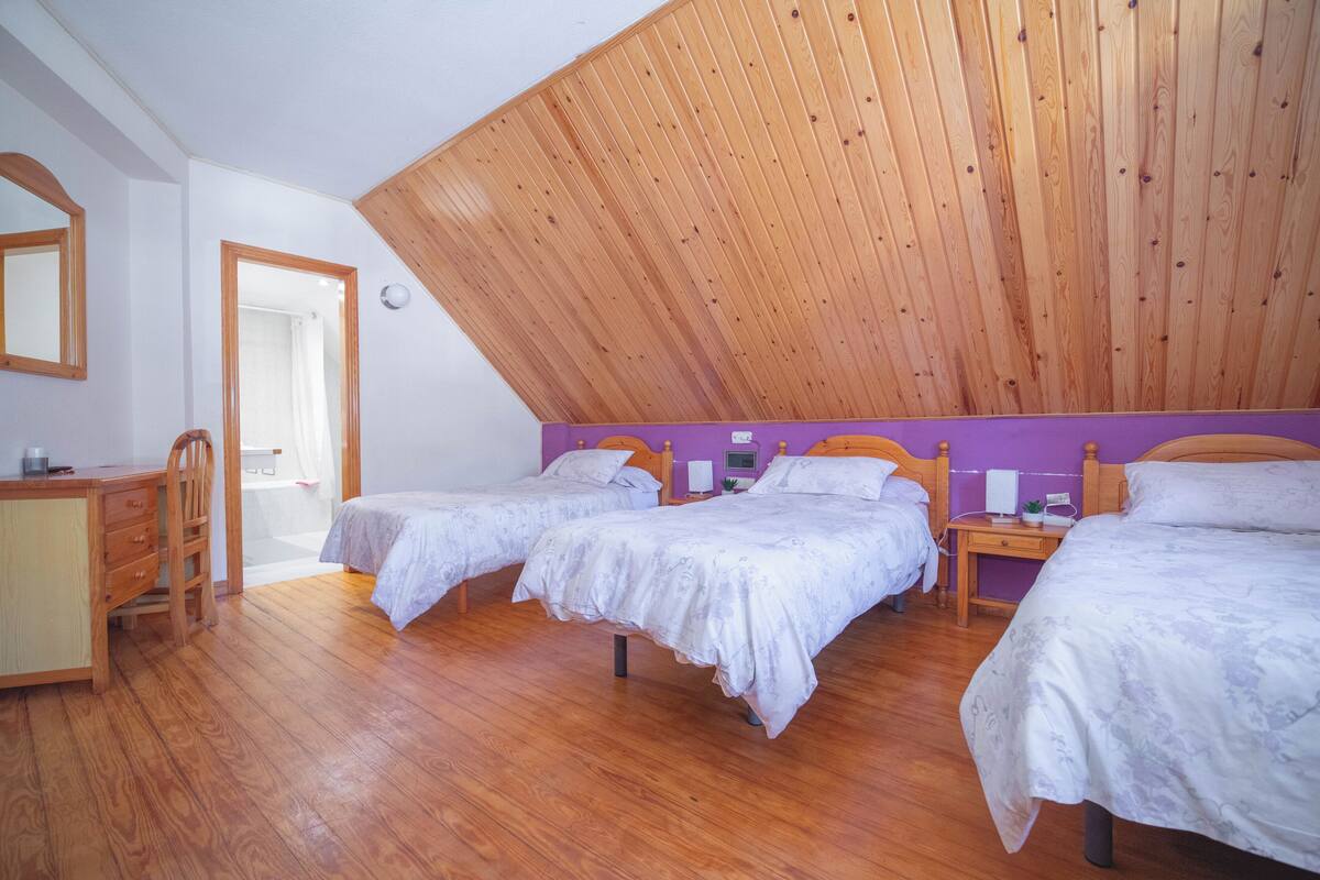 Ein Schlafzimmer mit zwei Betten, Holzboden, geneigter Decke und einem kleinen Schreibtisch mit Stuhl.