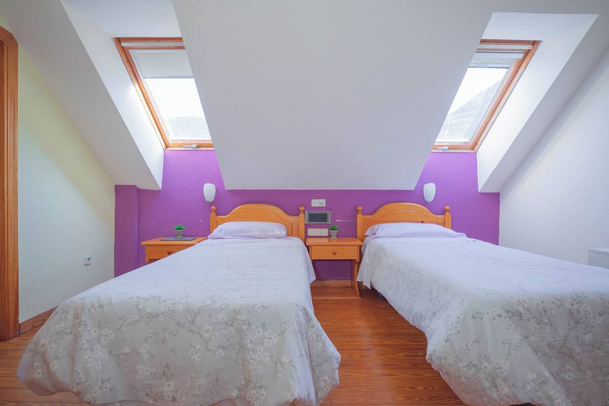 Ein Schlafzimmer mit zwei Betten, einem Nachttisch, einem kleinen Tisch und einem Fenster.