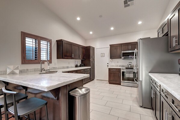 A modern kitchen with a large island, stainless steel appliances, and dark wooden cabinets. - 5 Bdrm Entertainers Dream Home. Game Room, HTD Pool and Backyard Oasis! (Scottsdale)