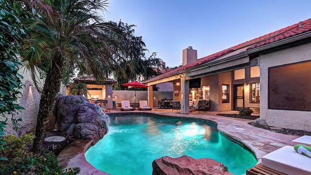 A swimming pool with a stone border, surrounded by lounge chairs and a covered patio area. - 5 Bdrm Entertainers Dream Home.  Game Room, HTD Pool and Backyard Oasis! (Scottsdale)