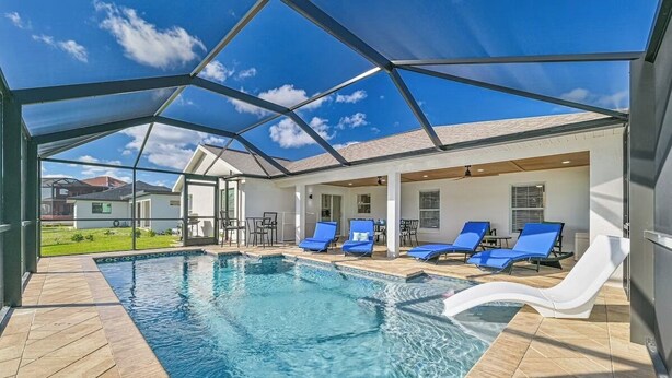A swimming pool with blue lounge chairs and a covered patio area. - Waterfront 3-Bed Home in SW Cape Heated Saltwater Pool, Boat Dock, Kayaks, Bikes (Cape Coral)