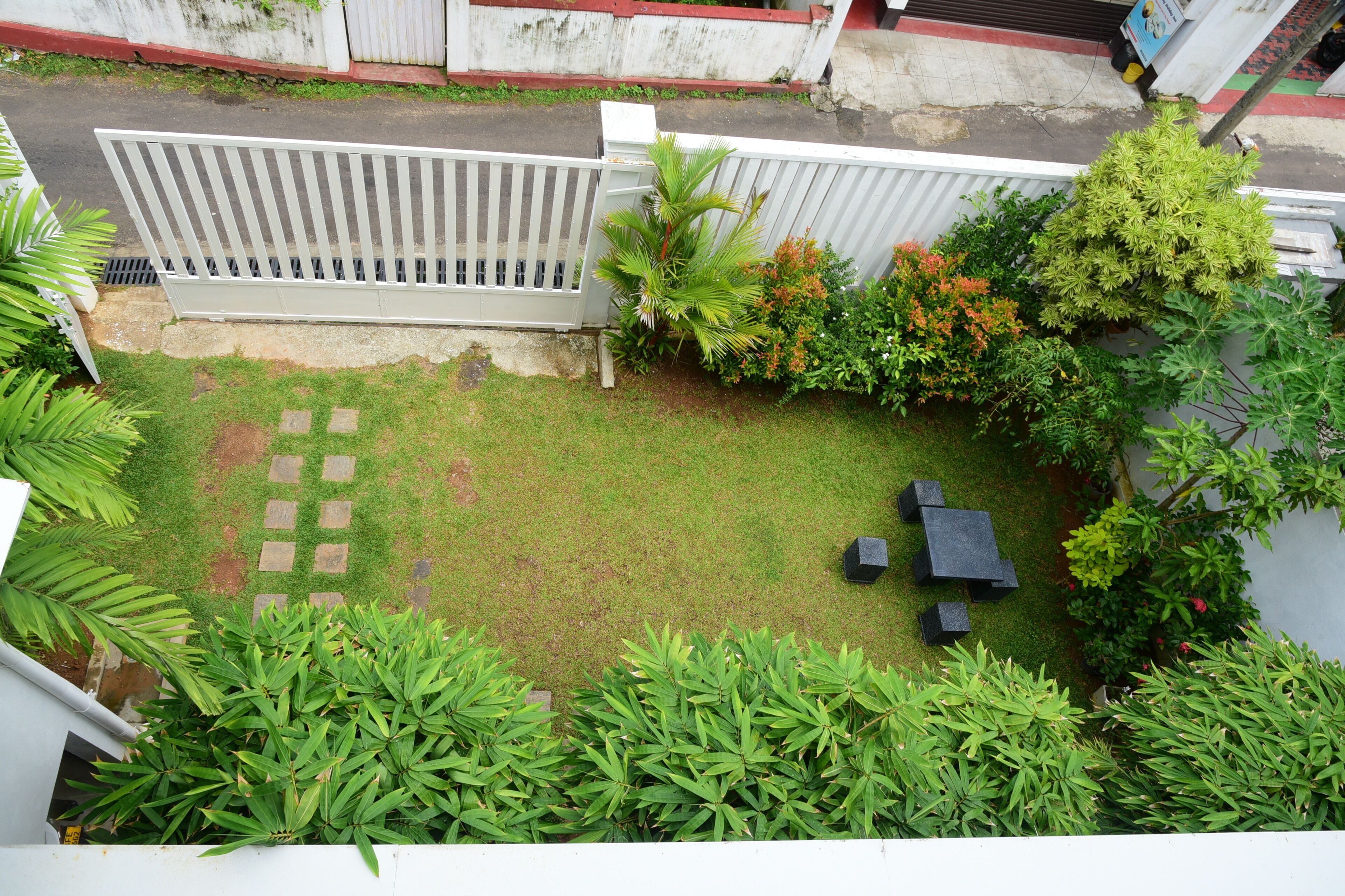 Un jardin avec une zone dallée, une clôture blanche et diverses plantes.