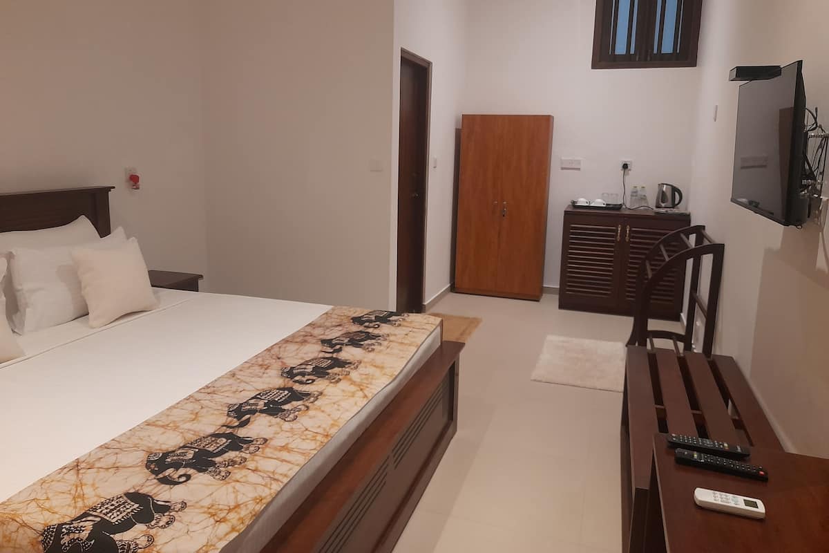 A bedroom with a bed, a wooden wardrobe, a desk with a chair, and a television mounted on the wall.
