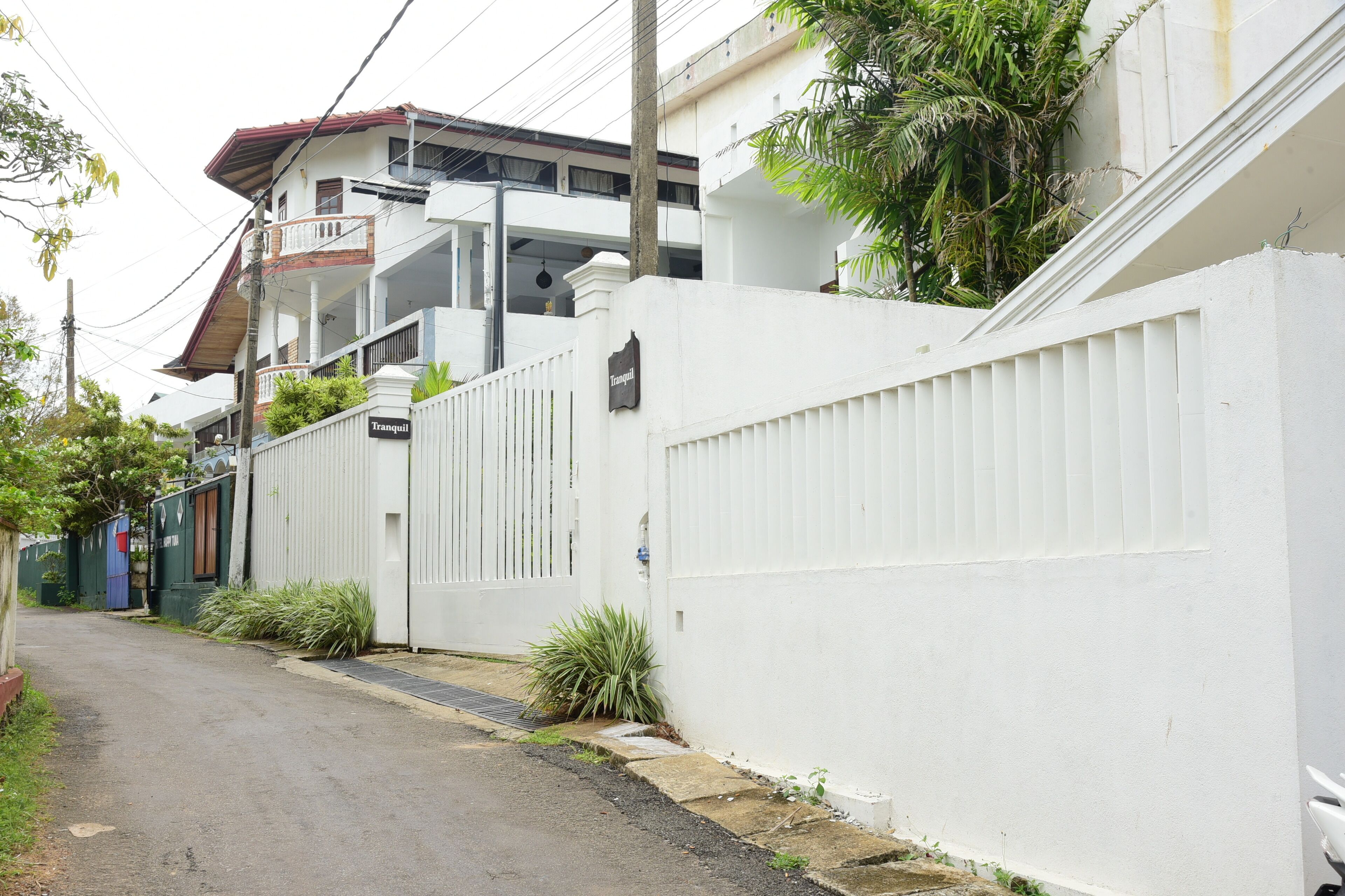 A narrow street with a white fence, a gated entrance, and a building with balconies.