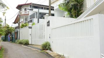 A narrow street with a white fence, a gated entrance, and a building with balconies.
