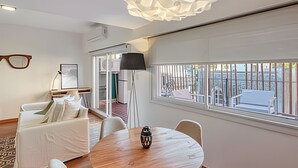 A modern living room with a round wooden table, white sofa, and a large window with a view of buildings. - Spacious with Terrace and Private BBQ in Belgrano (Buenos Aires)