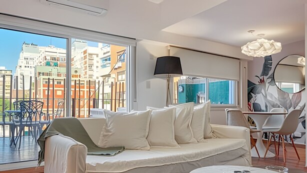 A modern living room with a sofa, a round coffee table, and a large window offering a city view. - Spacious with Terrace and Private BBQ in Belgrano (Buenos Aires)