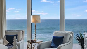 A room with a view of the ocean, featuring two armchairs, a lamp, and a small round table.