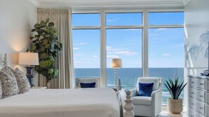 A hotel room with a large bed, a chair, a dresser, and a view of the ocean.
