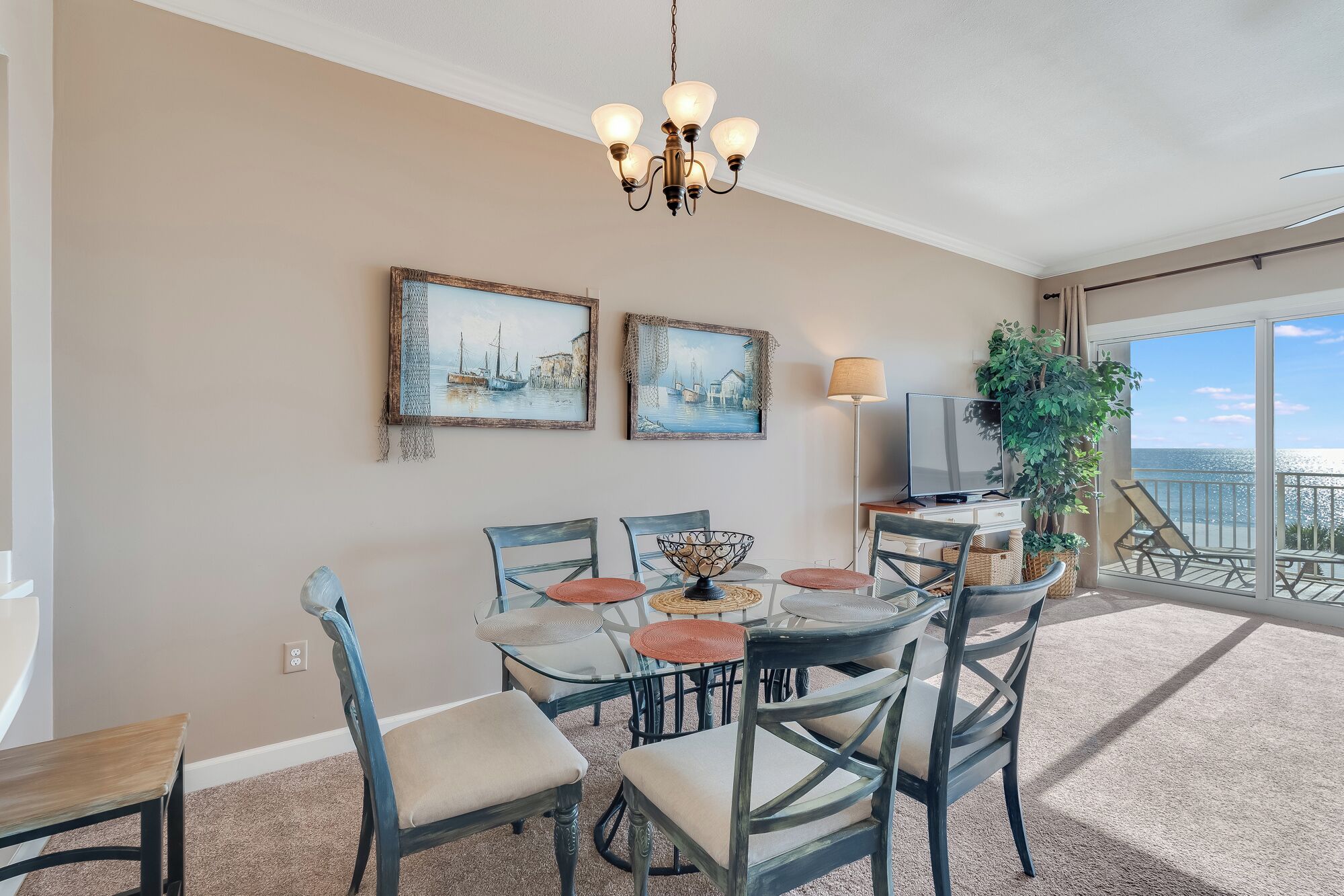 A dining area with a chandelier, two framed artworks, a television, and a balcony with a view.