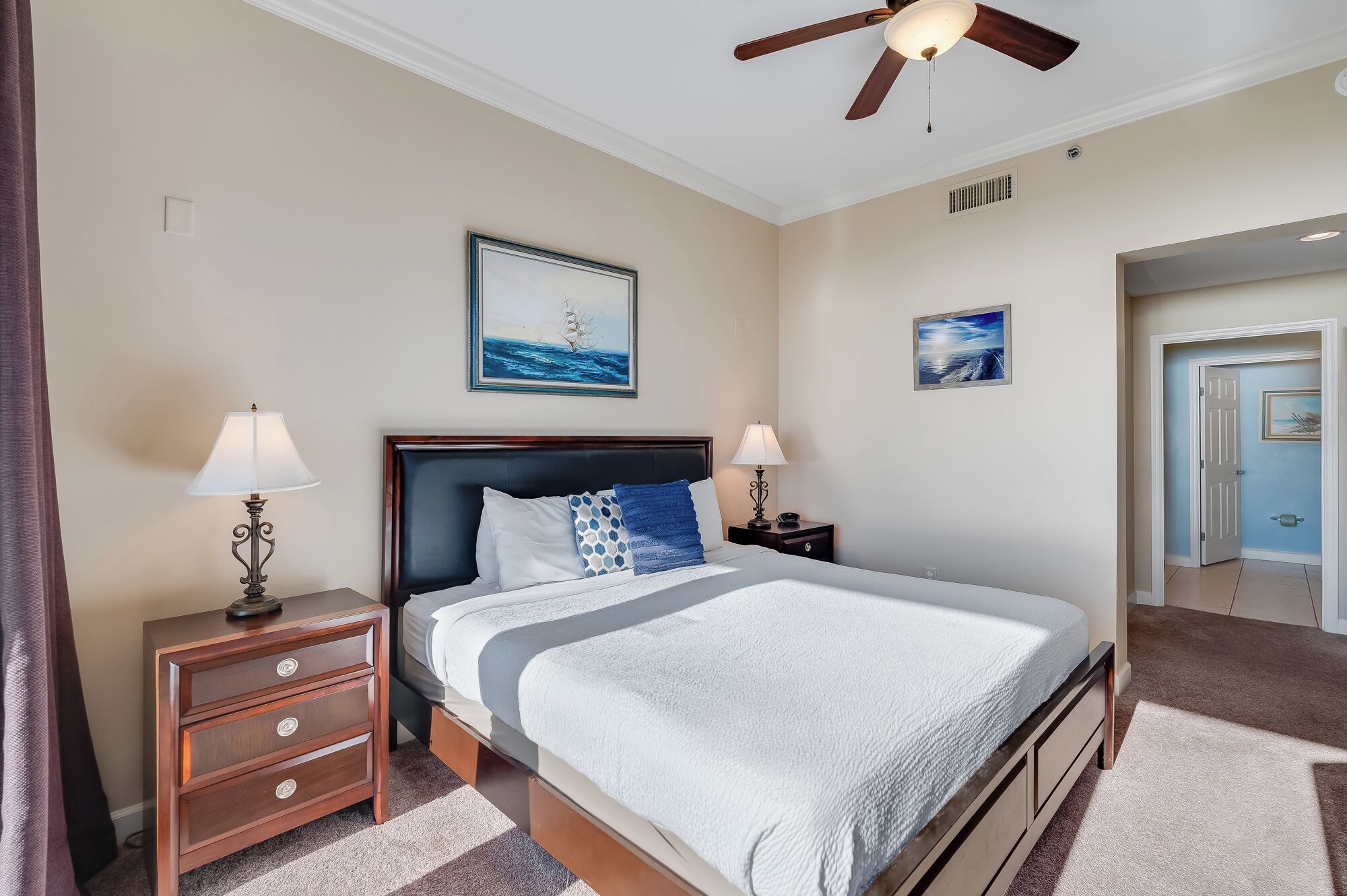 A hotel room with a bed, two bedside tables, a ceiling fan, and artwork on the walls.