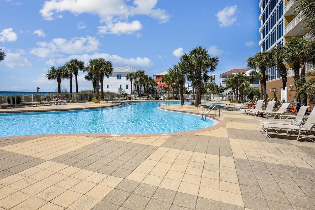 A pool area with lounge chairs, palm trees, and a view of the ocean.