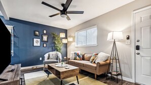 A modern living room with a blue accent wall, a ceiling fan, a sofa set, a coffee table, and a floor lamp. - AT&T & In the heart of it ALL! (Arlington)