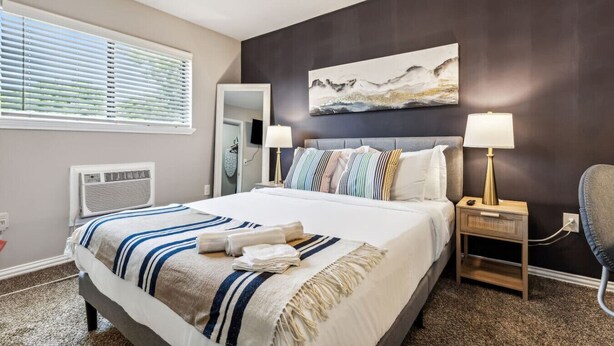 A neatly arranged hotel room with a large bed, two bedside lamps, a painting on the wall, and a window with blinds. - AT&T & In the heart of it ALL! (Arlington)