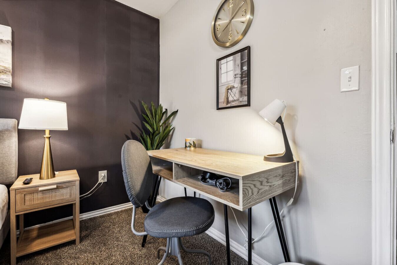 Ett litet kontorsutrymme med ett skrivbord, två stolar, en lampa, en klocka och en liten växt.