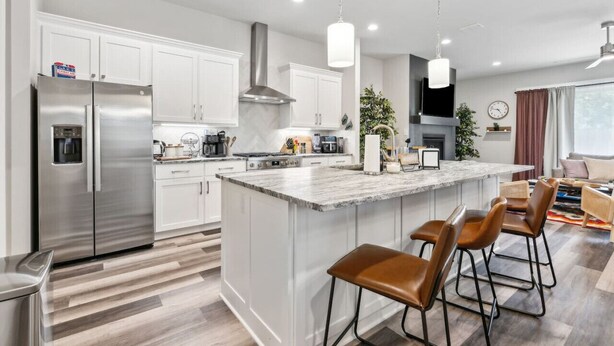 A modern kitchen with white cabinets, stainless steel appliances, and a marble island with bar stools. - Joyous 3BDTownhouse:  UltraCool & Spacious! (Fort Worth)