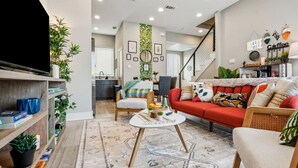 Un salon moderne avec un canapé, une table basse et un téléviseur. Un escalier mène à un autre niveau.