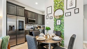 Une cuisine moderne dotée d’appareils électroménagers en acier inoxydable, un coin repas avec une table ronde et des chaises, et un mur orné d’œuvres d’art encadrées et d’un miroir.