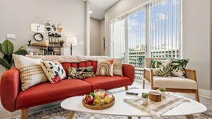 Un salon avec un canapé rouge, une table basse blanche et une vue sur la ville grâce à de grandes fenêtres.